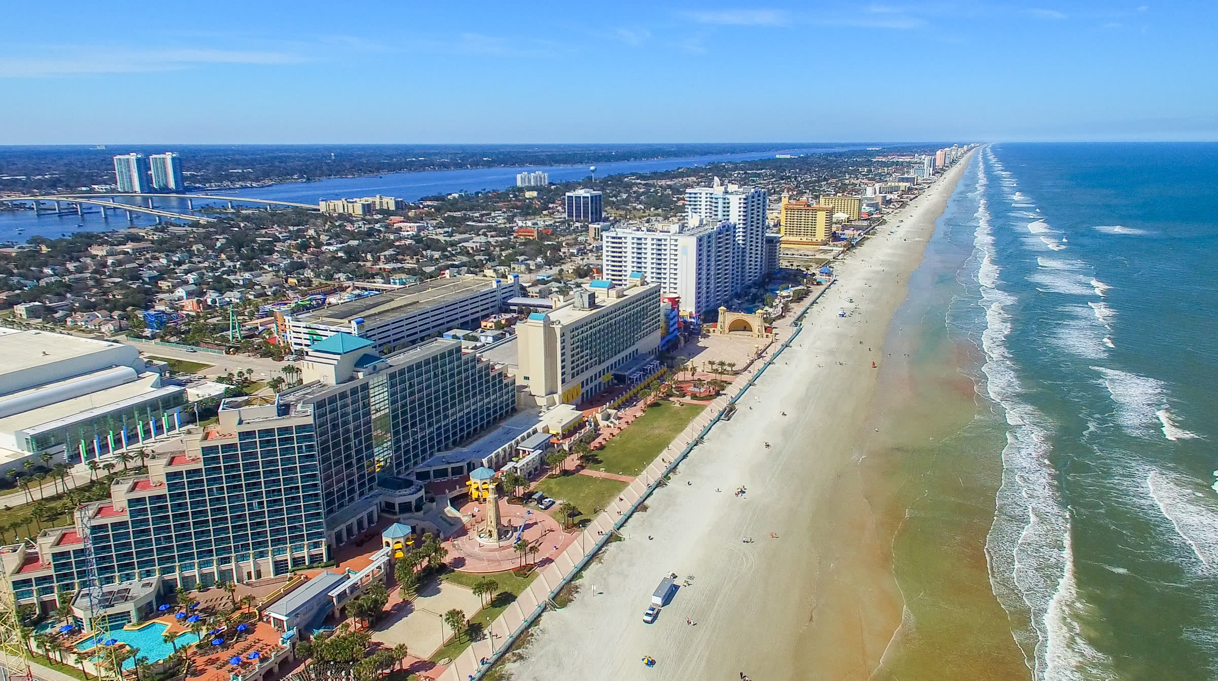 An aerial view along a high-rise beachfront, with a bridge and inland waterway beyond
